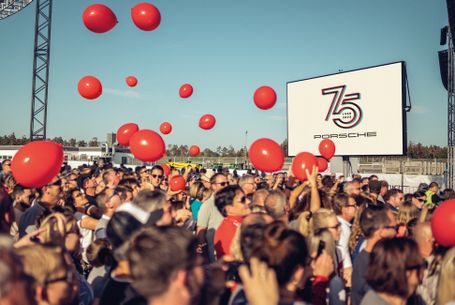    		Porsche Deutschland feiert „Festival of Dreams“ am Hockenheimring - Feiernde Menschenmenge, Luftballons steigen auf, Porsche 75 Jahre Logo